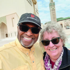Richard Cambridge ’70 and a fellow alum smile together outdoors, both wearing sunglasses, celebrating their connection through the Macalester Alumni Board.
