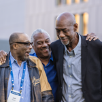 A group of alumni laugh and embrace each other outside during Mac Fest 2025.