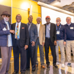 A group of alumni smile together on stage during an event at Mac Fest 2025.