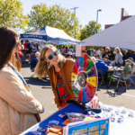 Attendees interact at a prize wheel activity table during the M Club Cookout at Mac Fest 2025.