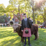 A bagpiper poses with Hartnett the mini Highland Coo on the Great Lawn at Mac Fest 2025.