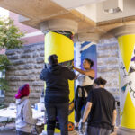 Students apply yellow paint to a column outside DeWitt Wallace Library