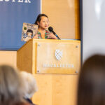 Kao Kalia Yang speaks at a podium and holds up her book, The Rock in My Throat