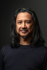 Assistant Professor Randy Reyes poses against a dark background wearing a navy sweater.
