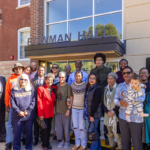 A large group of alumni and community members pose together in front of Bowman Hall during its dedication event at Mac Fest 2025.
