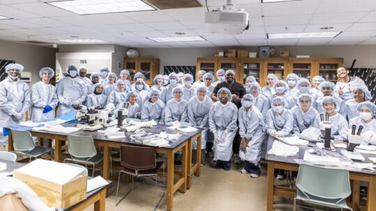 Dr. Malik Mays ’19 stands with a group of Macalester students in the lab.