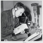 A student wearing 1950s headphones jots notes on a notepad while looking at a clipboard