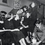 A student holds a 1940s microphone and leans in to speak to a group of eight students