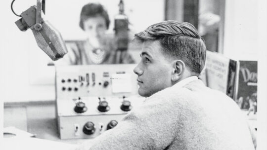 A 1960s photo of two students sitting in a radio booth and speaking into microphones