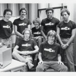 Seven students wearing 1979 WMCN shirts sit in a group and smile for the camera
