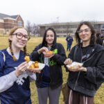 Three students smile at the camera while holding food from a food truck