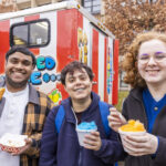 Three students hold food from a food truck and smile