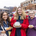Three students smile for the camera, one holding a boxed cake