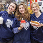 Three students hold food from a food truck and smile