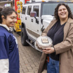 Student holds up a boxed cake while another student laughs