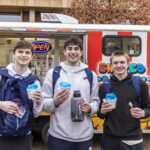 Three students hold snow cones and smile in front of a food truck