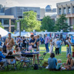 A group of Reunion attendees, including small children, sit and talk on the Great Lawn with food trucks in the distance
