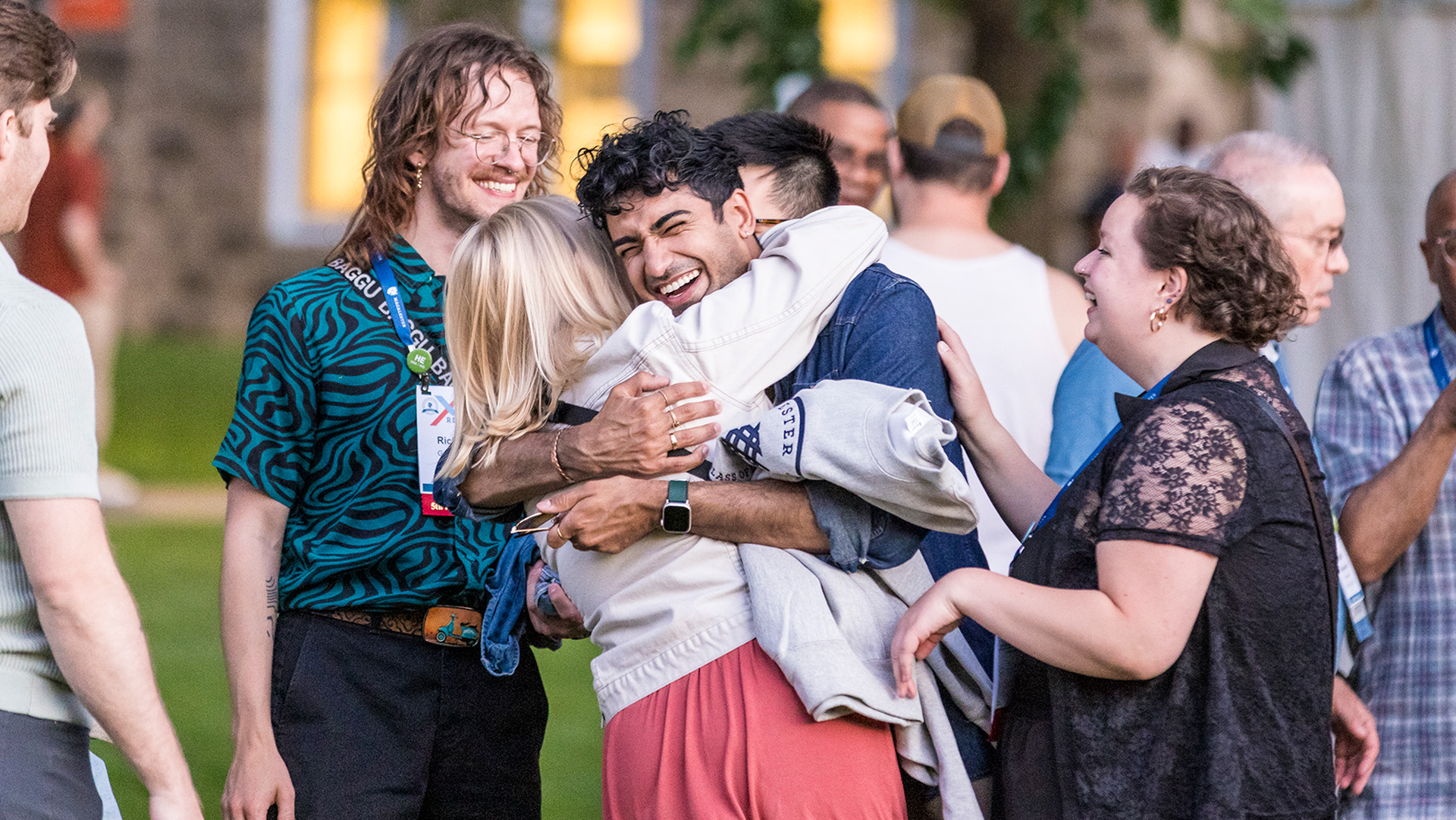 Two alumni smile and hug each other in a group of other alumni