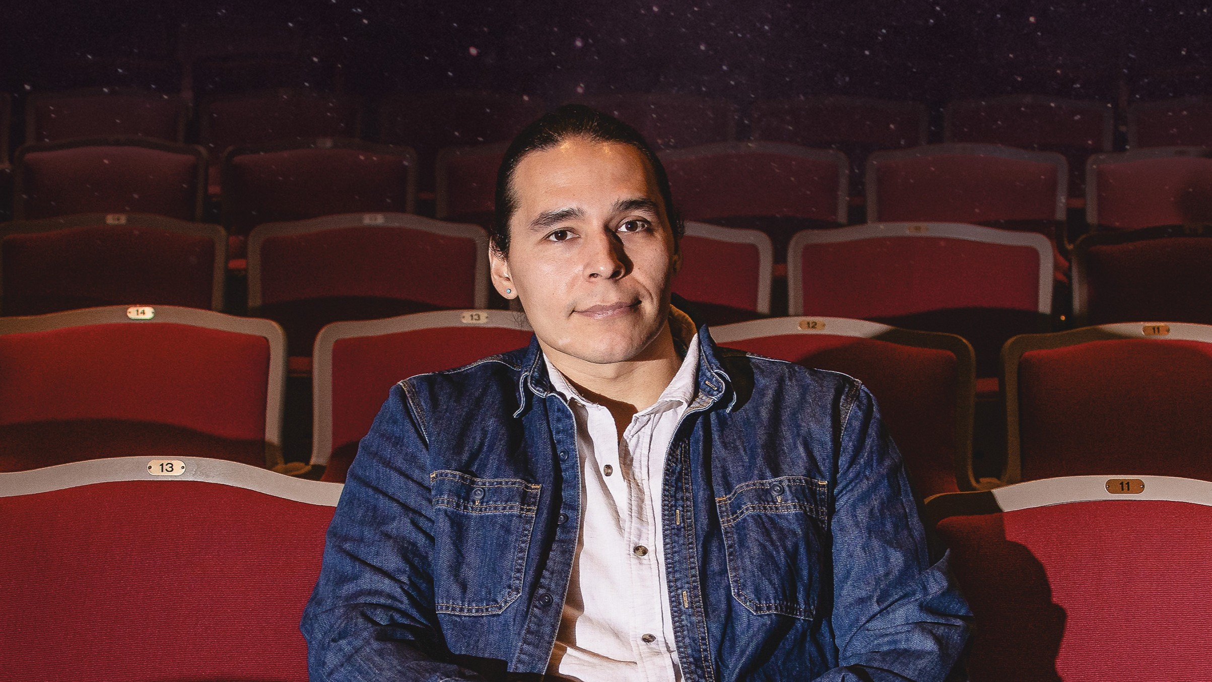 Ajuawak Kapashesit ’13 poses for a headshot in a movie theater seat.