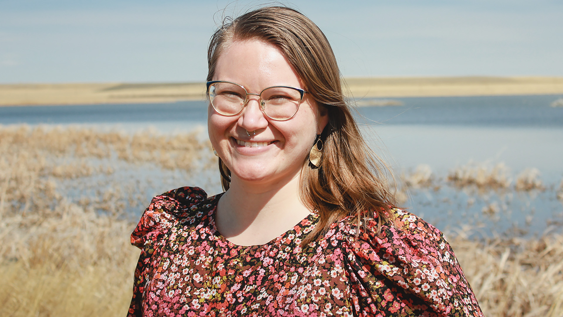 Abaki Beck '15 stands in front of a lake surrounded by prairie grasses