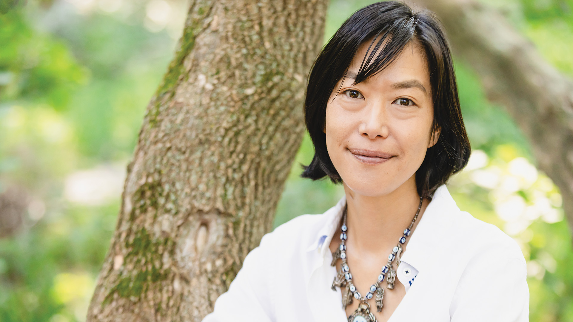 Headshot of Masami Kawazato '00 sitting in front of a tree in a grassy park on a sunny day