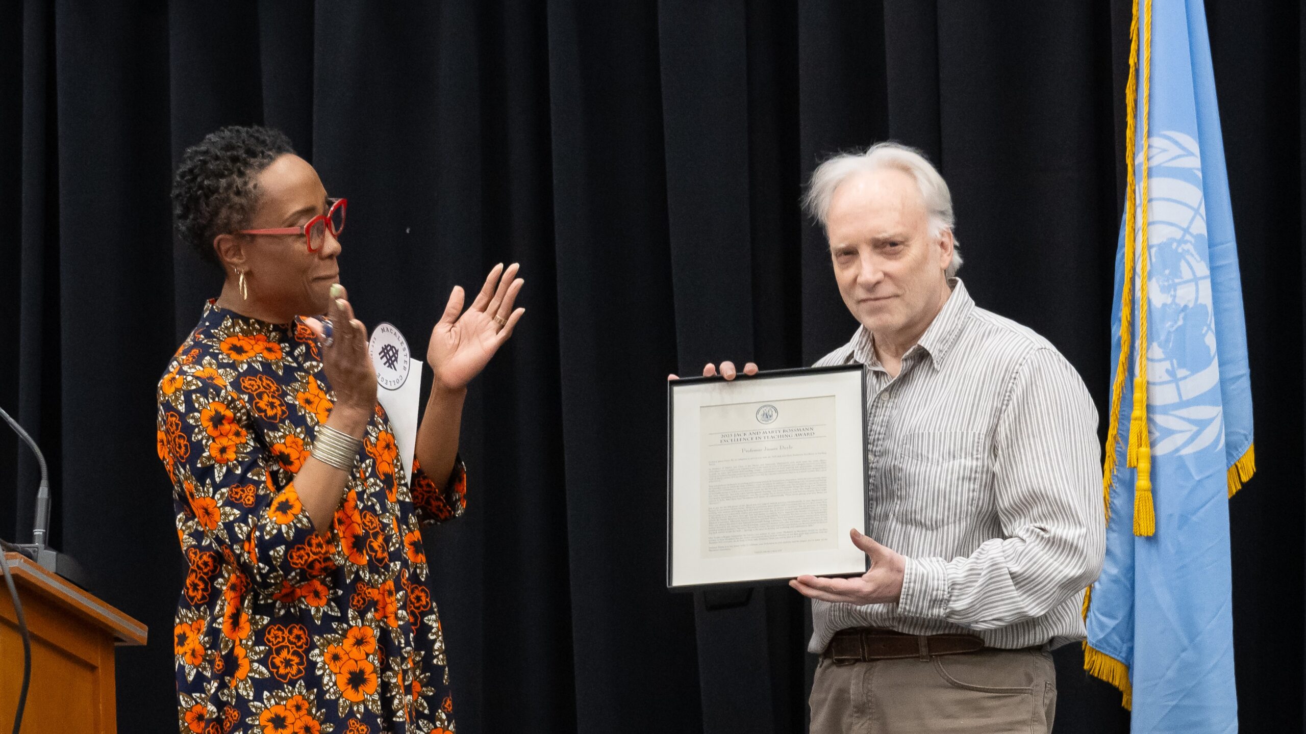 Professor James Doyle holds his 2025 Jack and Marty Rossmann Excellence in Teaching Award. Executive Vice President and Provost Lisa Anderson-Levy applauds next to him.