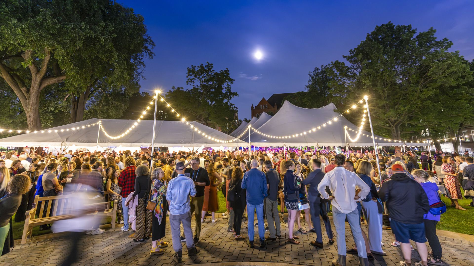 A wide crowd of alumni gathered under moonlight and glowing tent lights during the evening Tartan Toast celebration.