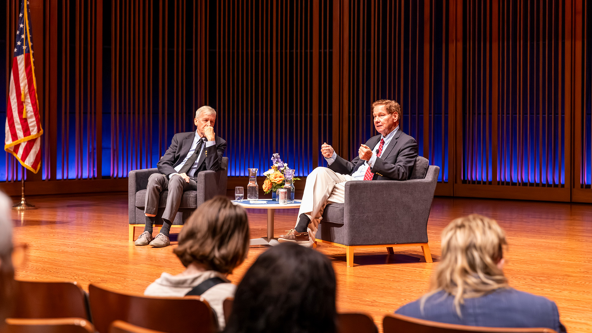 Two former US representatives sit across from each other in the middle of a stage, engaged in discussion.