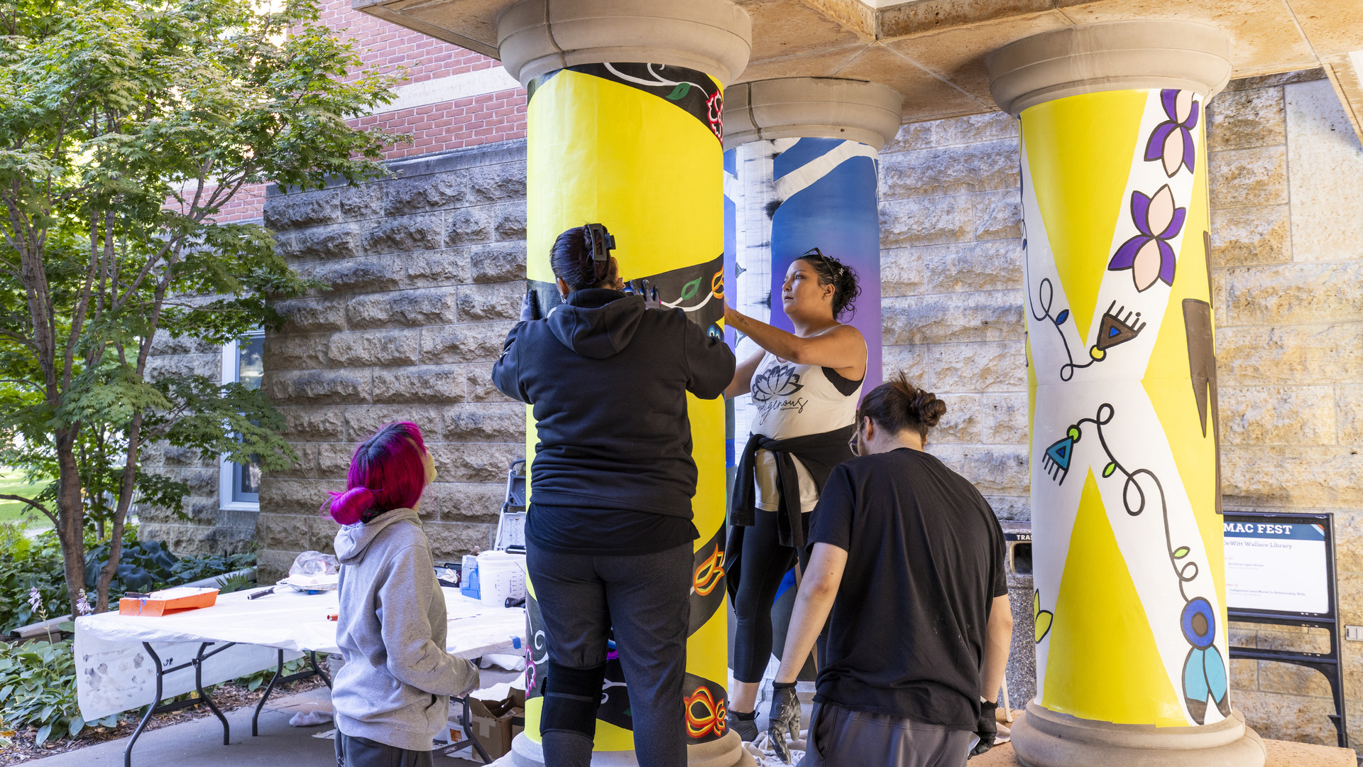 Students apply yellow paint to a column outside DeWitt Wallace Library