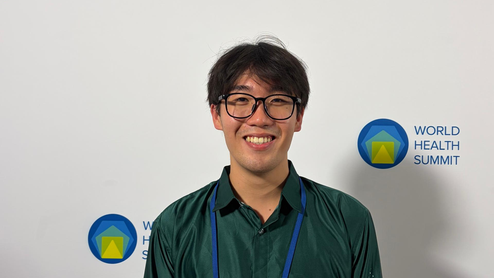 Macalester student Mo Chang ’29 smiles in front of a World Health Summit backdrop.