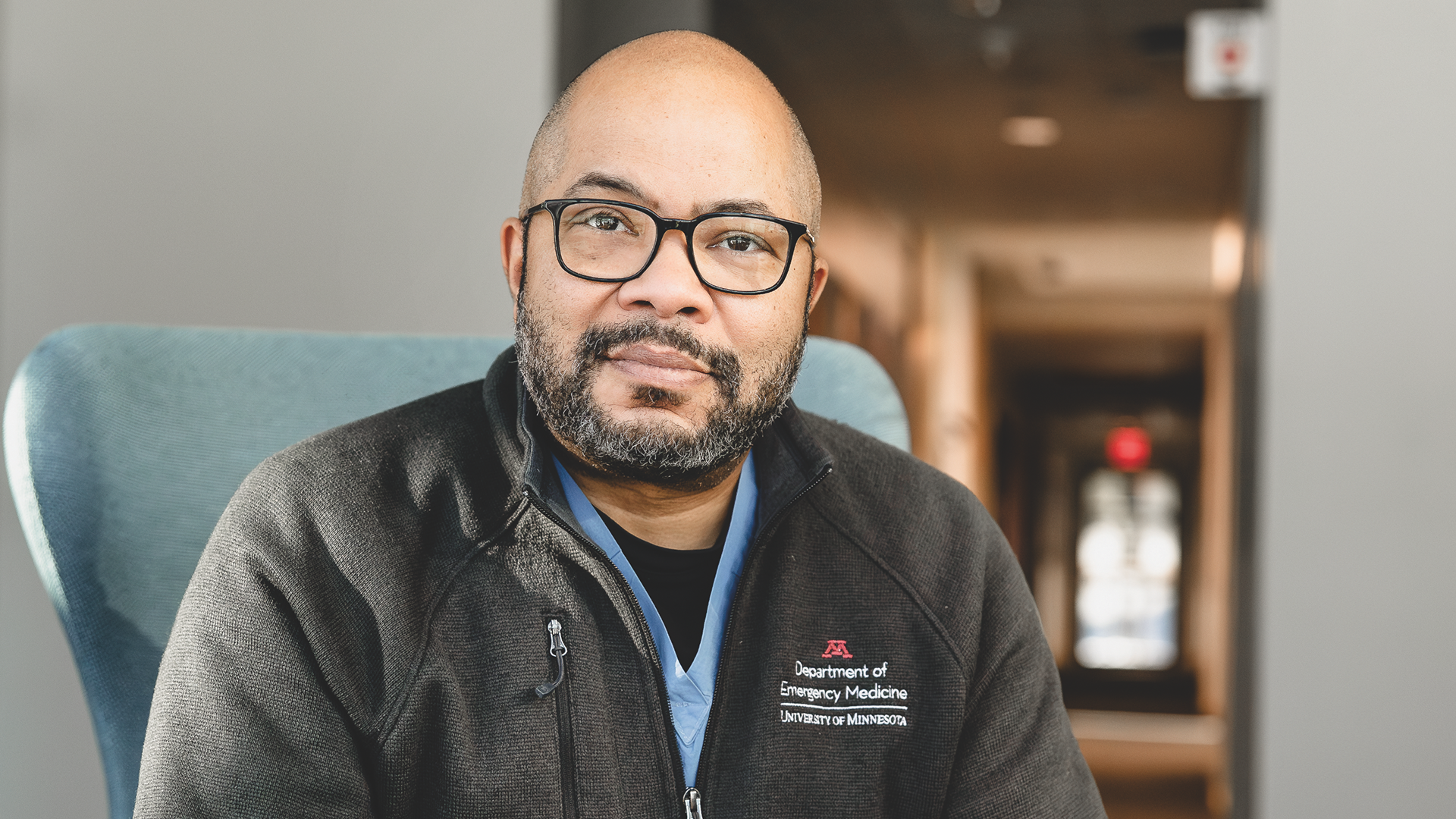A close-up portrait of Macalester alumnus Dziwe Ntaba ’95, an emergency medicine physician, wearing glasses and a dark University of Minnesota medical fleece.