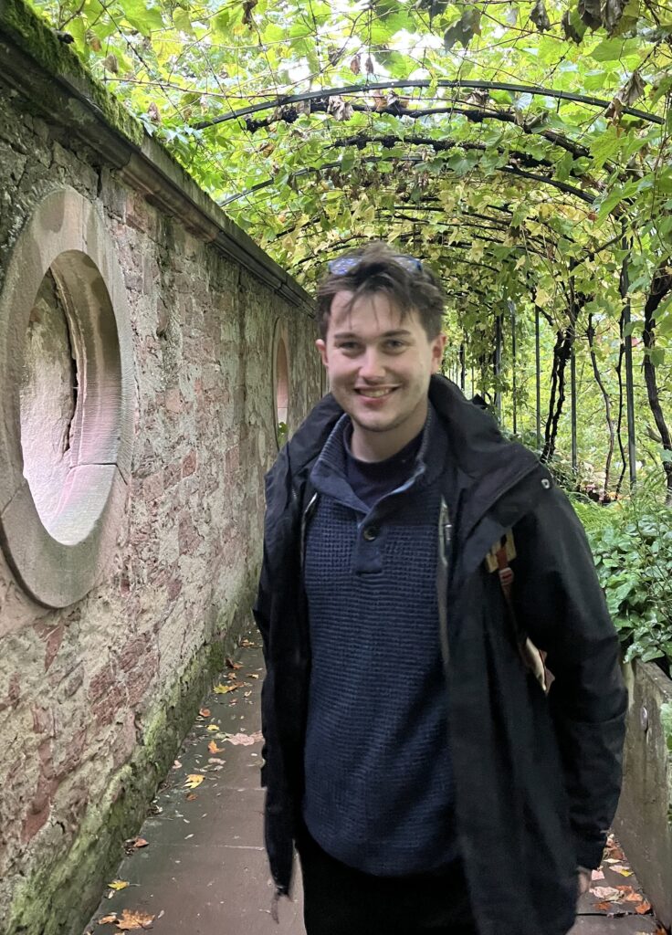Ryan Connor ’25 poses for a portrait in front of a tree-lined pathway.