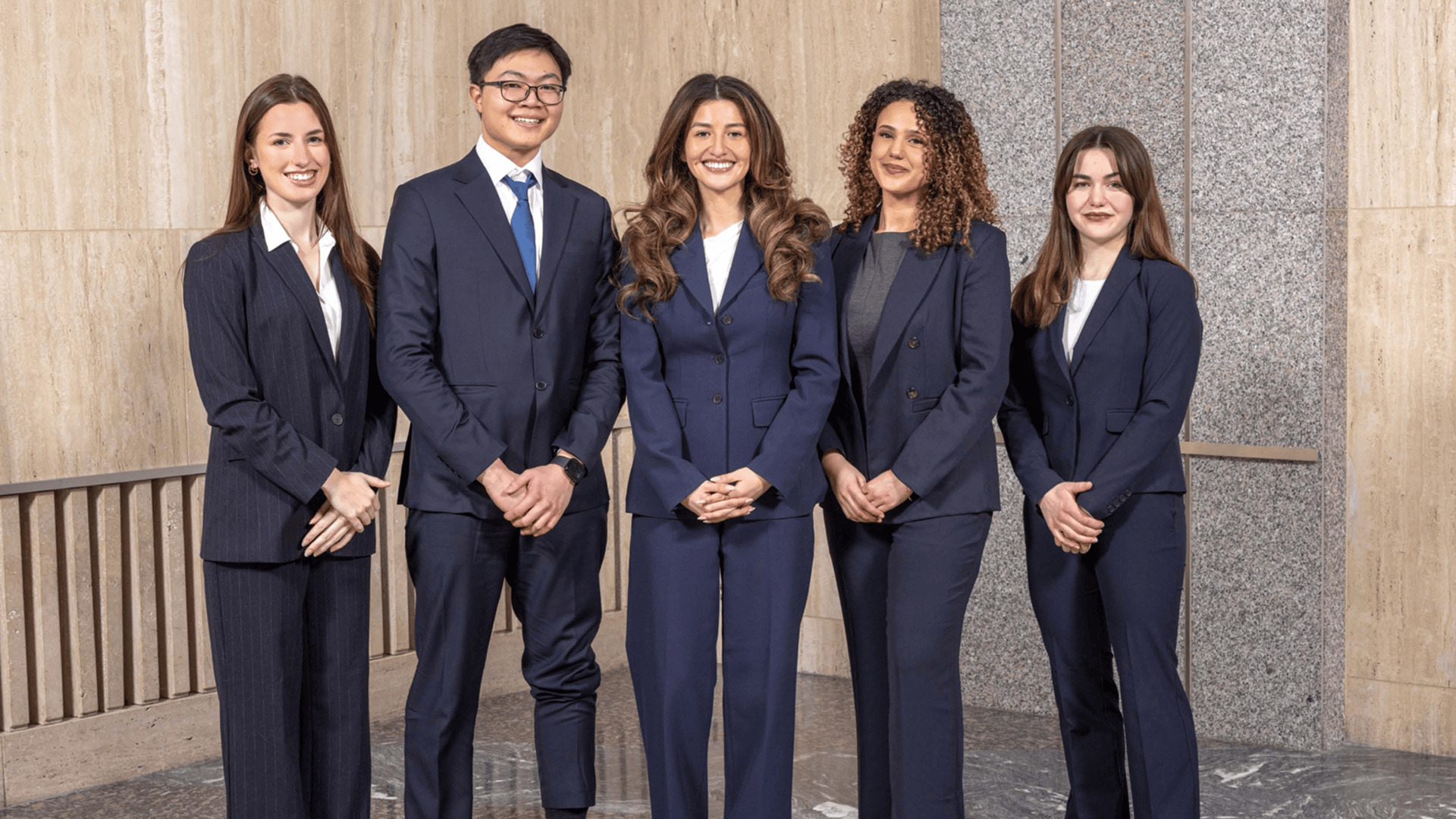 Four Macalester students and one St. Thomas MBA student stand in a row in a corner of a room at Mayo Clinic in Rochester and smile at the camera.