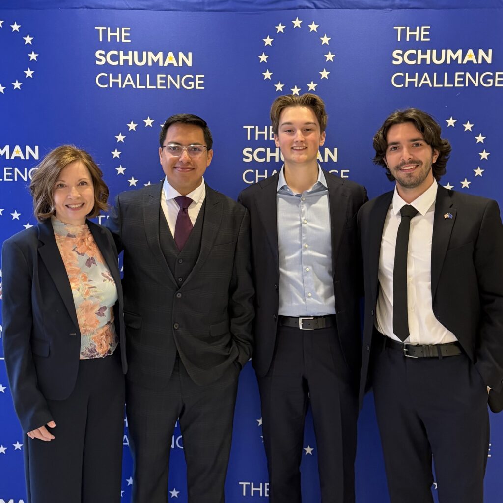 Three students and a professor stand in front of a blue backdrop that says THE SCHUMAN CHALLENGE