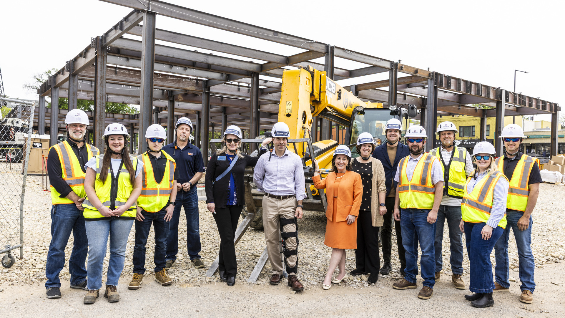 President Rivera and a group wear hard hats and stand in front of the under-construction residence hall and welcome center
