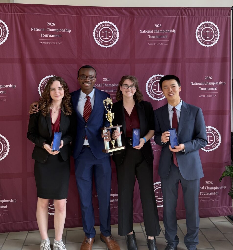 All-American winners Ainsley Meyer, Kate Caulder and Jo-Z Wu hold their All-American distinction awards and pose with Kofi Anyimadu in front of a maroon backdrop at the American Mock Trial Association’s 41st National Championship Tournament in Washington, DC.