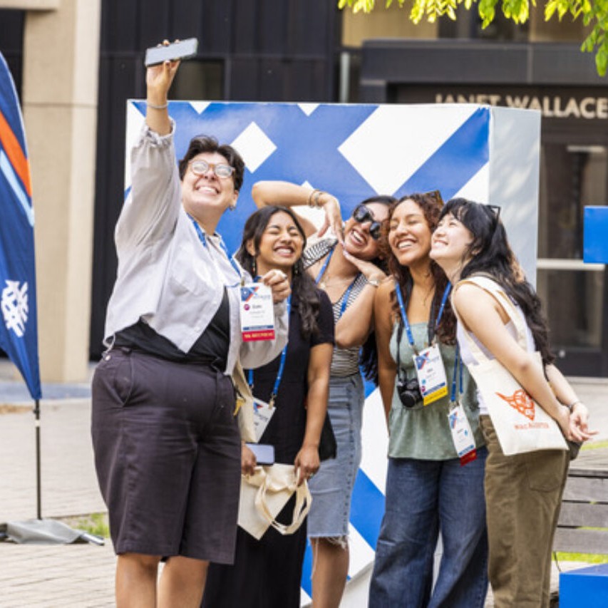 Five alumni take a selfie in front of statue of Macalester shield
