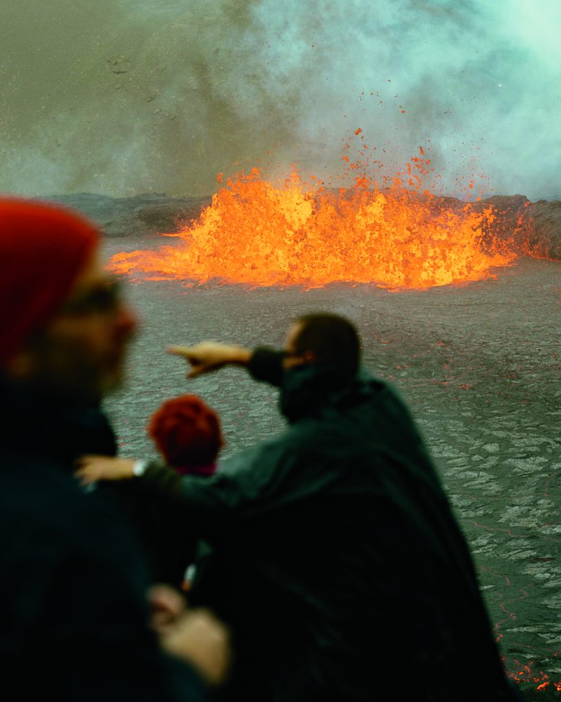 A volcano on Reykjanes Peninsula erupts, with a number of onlookers blurred in the foreground.