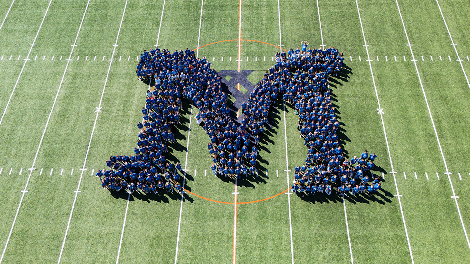 The Class of 2030 stands together in an M shape on the football field