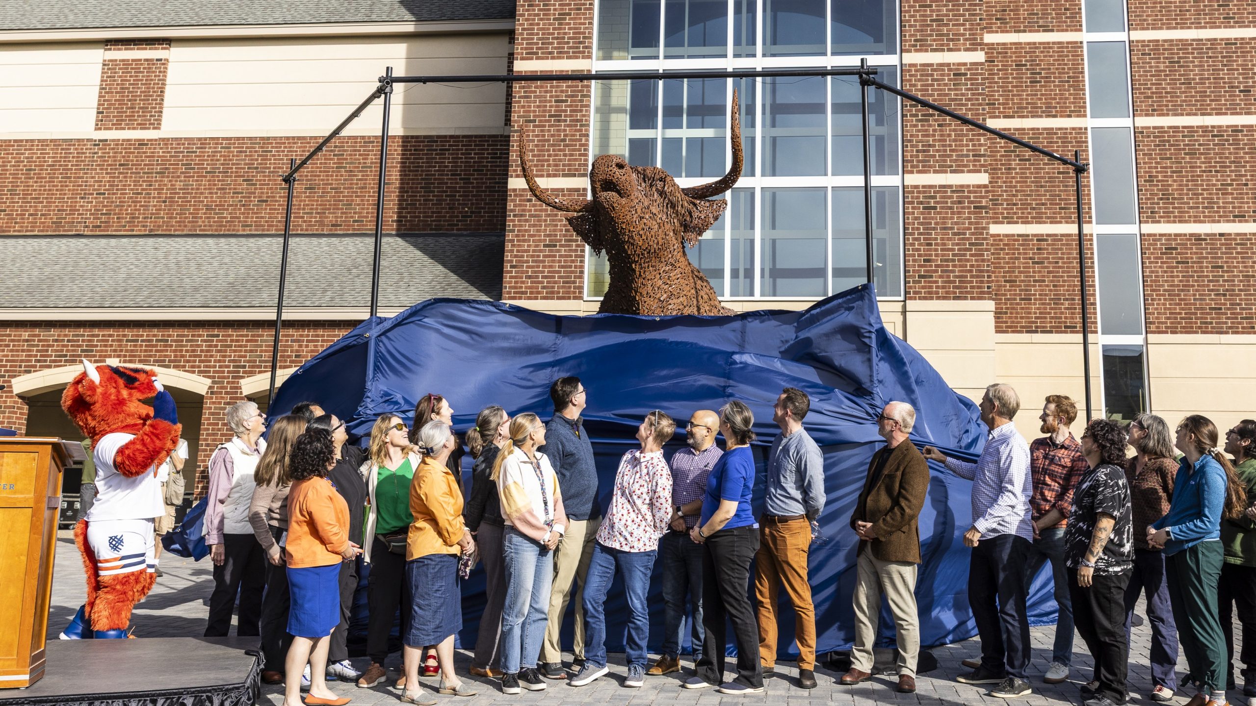 Faculty staff in front of the new Coo sculpture as its unveiled at a ceremony during Mac Fest.