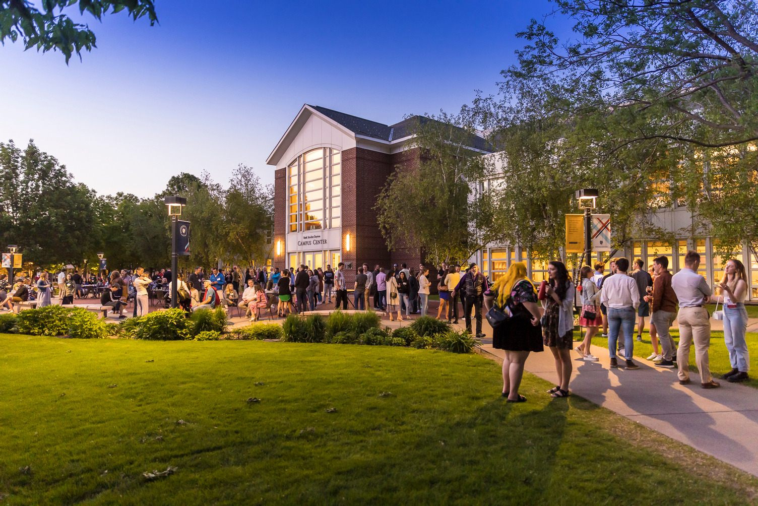 A large group of alumni stand outside the Campus Center in the evening during Reunion.