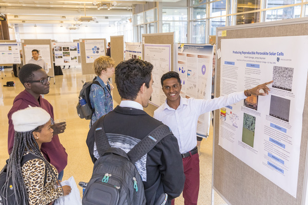 Student presents a physics research poster to a small group of other students