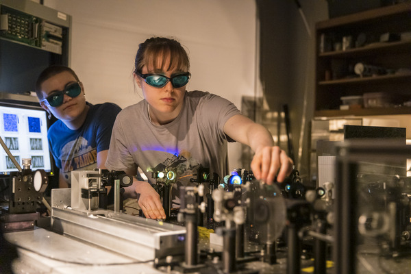 Two students wearing safety glasses control a small machine