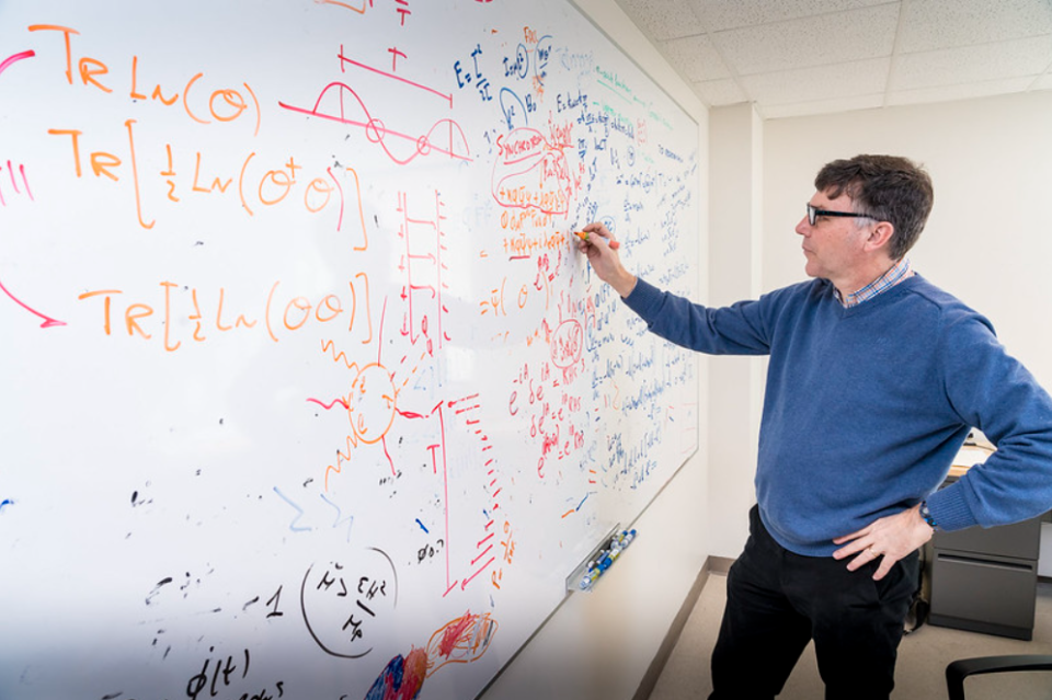 Professor writes equations on a whiteboard