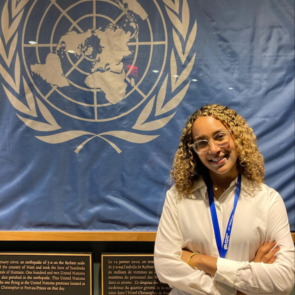 Amanda Nogueira Moreira de Souza stands in front of a UN flag