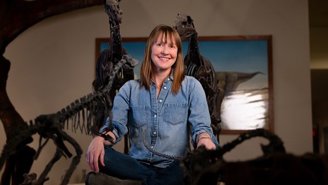 Kristi Curry Rogers poses next to dinosaur bones