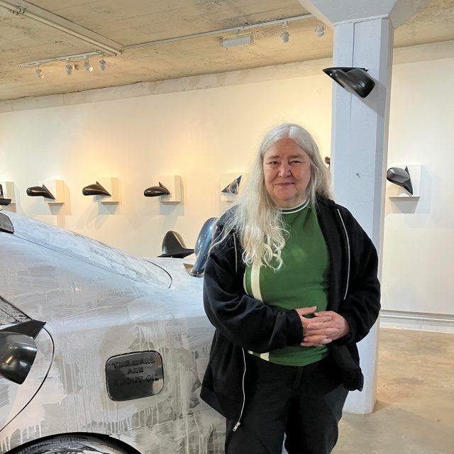 Prof. Ruthann Godollei stands next to a car covered in white paint.