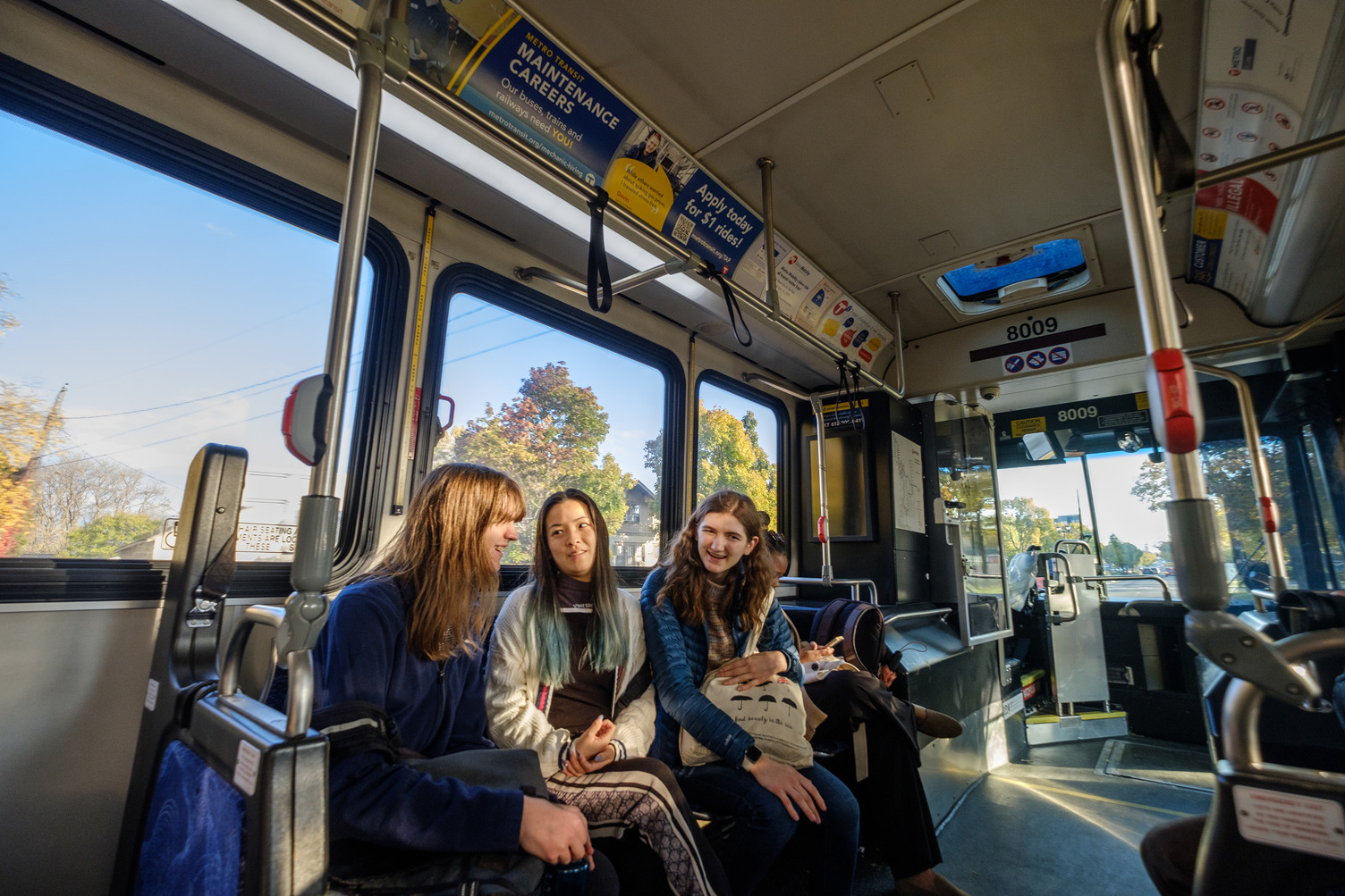 A group of Macalester students sit together on a Metro Transit bus, chatting and smiling.