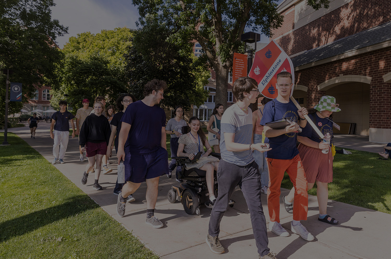 Students walk across campus in their orientation group. The leader is holding a sign with the name of their Scottish house, Elphinstone.