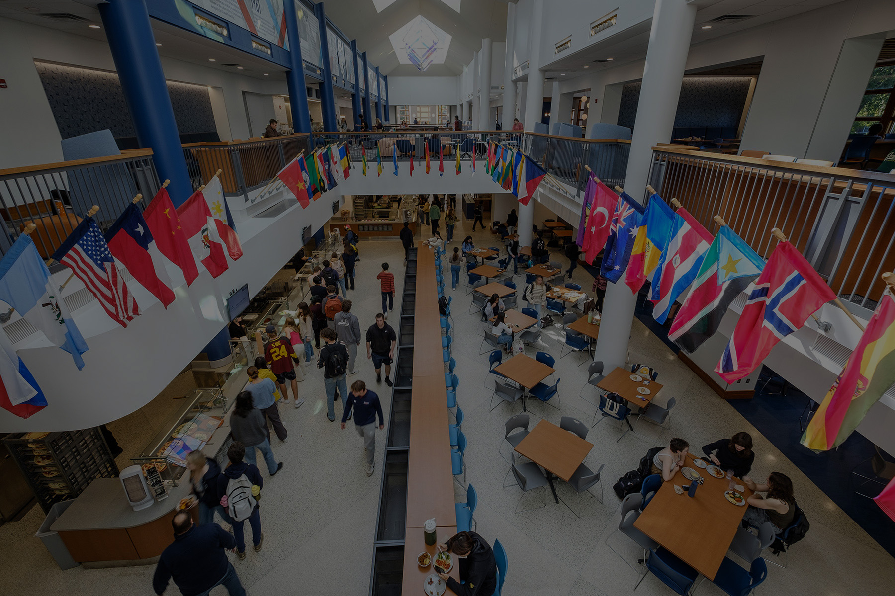 Macalester's Campus Center after the renovations. Students eat in Cafe Mac with international flags flying above them.